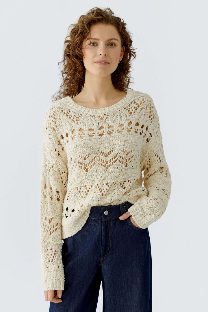 Chandail en maille ajourée beige avec motif texturé, coupe décontractée, encolure ronde porté avec un jean foncé. Féminin et raffiné.