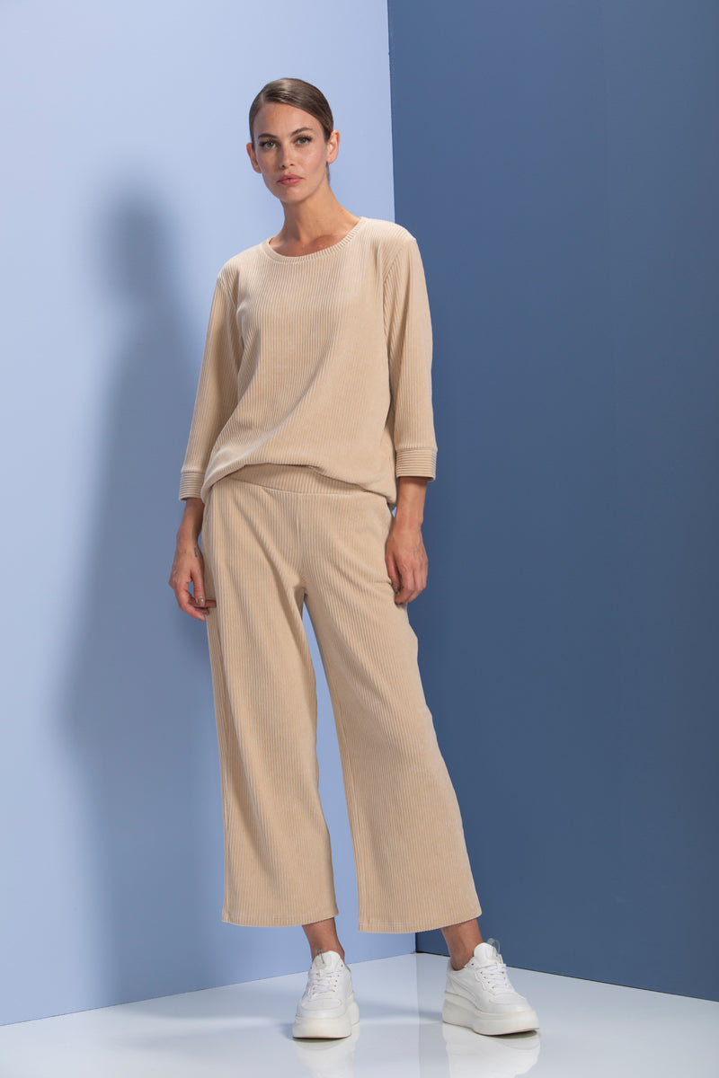 Femme portant un chandail en maille côtelée beige, coupe ample, manches trois-quarts, avec pantalon assorti, style moderne et confortable.