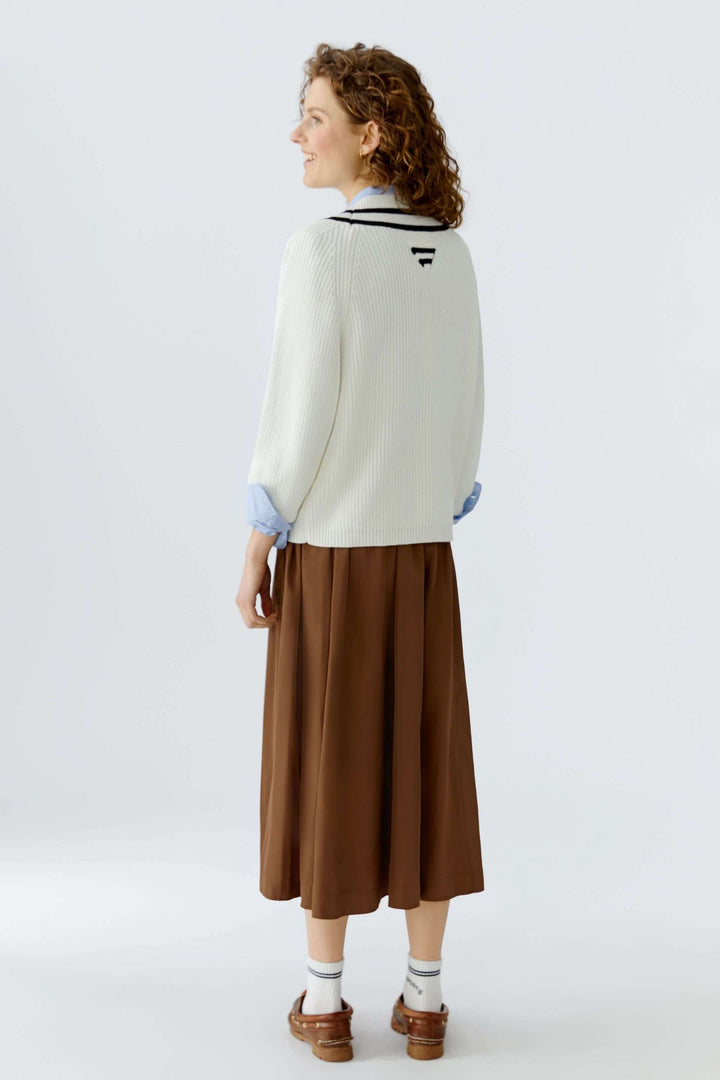 Chandail en maille encolure en V porté avec jupe marron pour un look chic et moderne, idéal pour superposition sur chemise bleue.