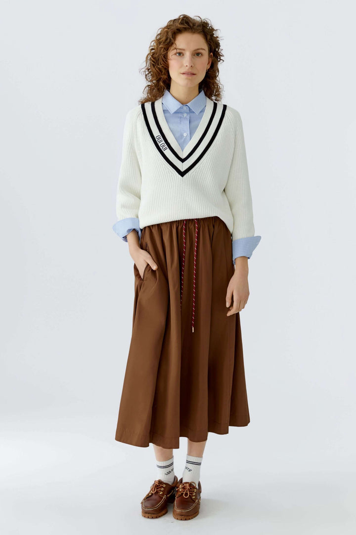 Femme portant un chandail en maille encolure en V avec chemise et jupe, ajoutant une touche moderne à une tenue classique.