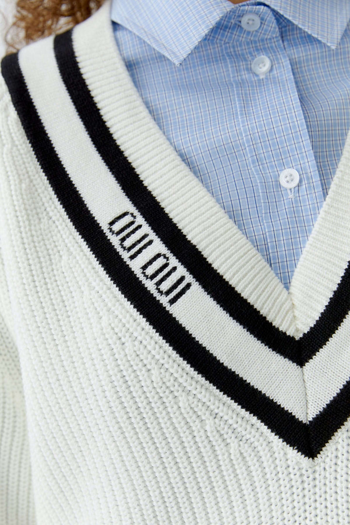 Chandail en maille encolure en V avec détail contrastant, porté sur une chemise bleue pour un look moderne et graphique.