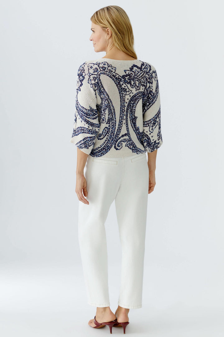 Femme portant un chandail en maille à motif cachemire, manches trois-quarts, sur un fond blanc, créant une allure chic et moderne.