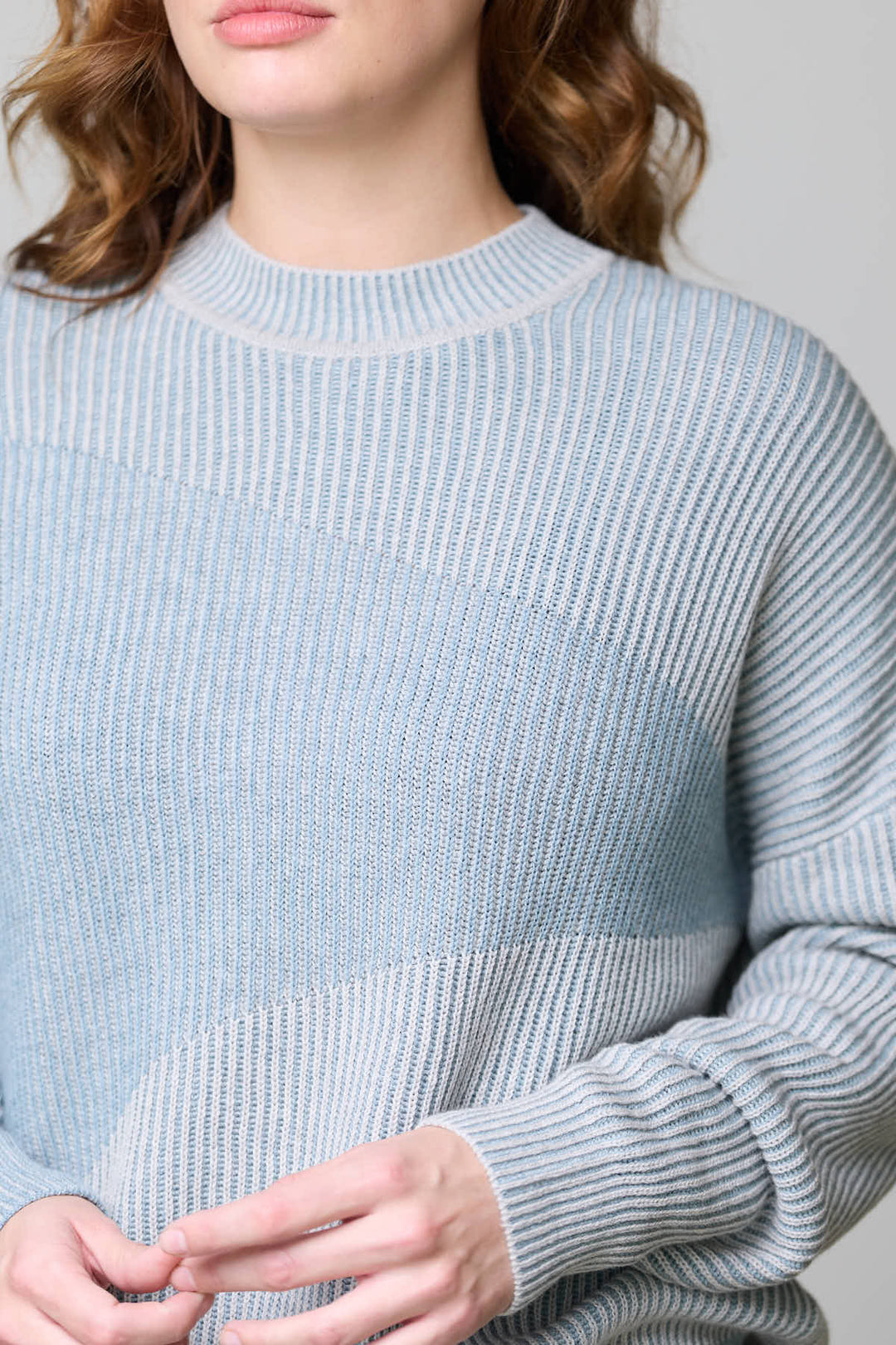 Femme portant un chandail en tricot côtelé bleu clair, texture raffinée, encolure ronde, coupe droite et ample, manches longues.