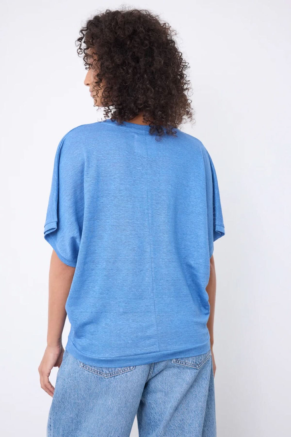 Femme portant un chandail à encolure en V bleu, coupe ample, manches larges, maille légère. Style décontracté avec jean.
