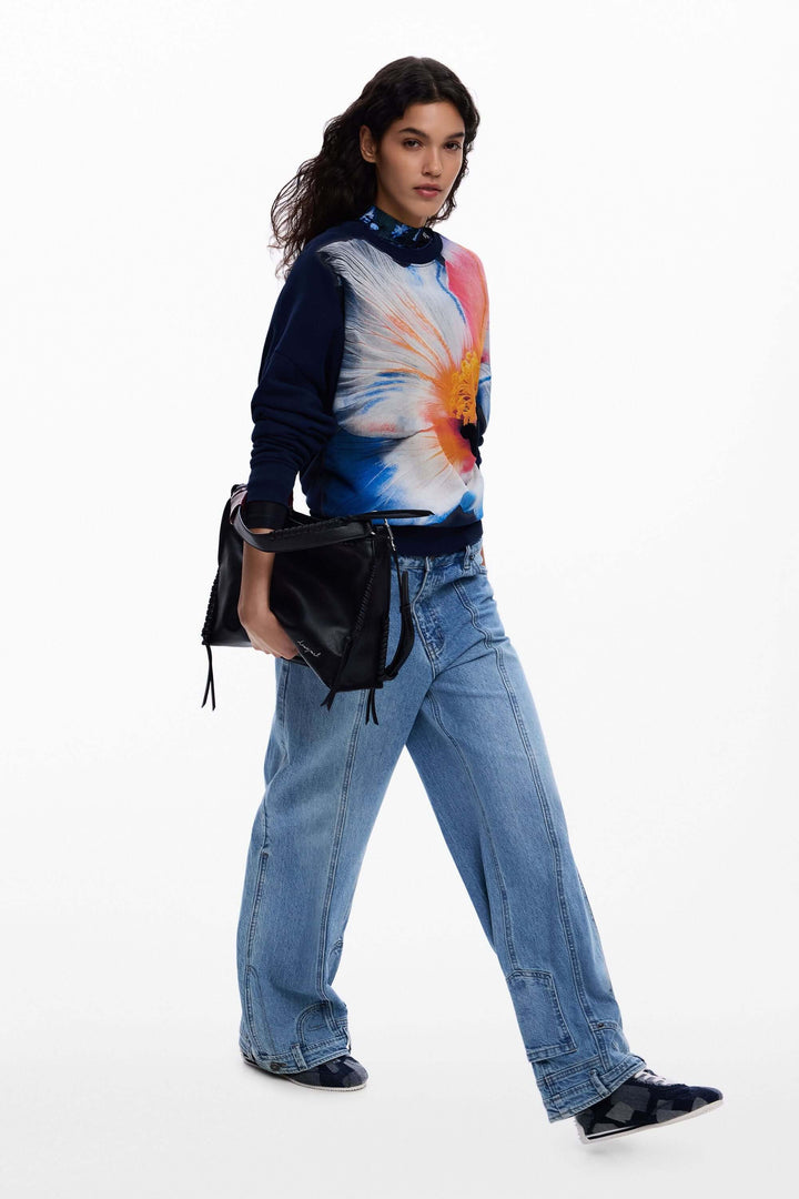 Chandail à grande fleur porté avec un jean, mettant en valeur le motif floral surdimensionné et les empiècements contrastants.