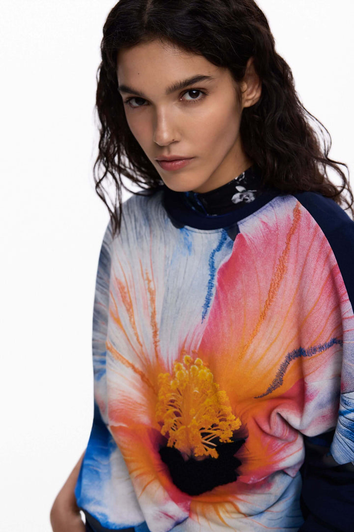 Femme portant un chandail à grande fleur avec un motif floral coloré et expressif, idéal pour un look moderne et stylé.