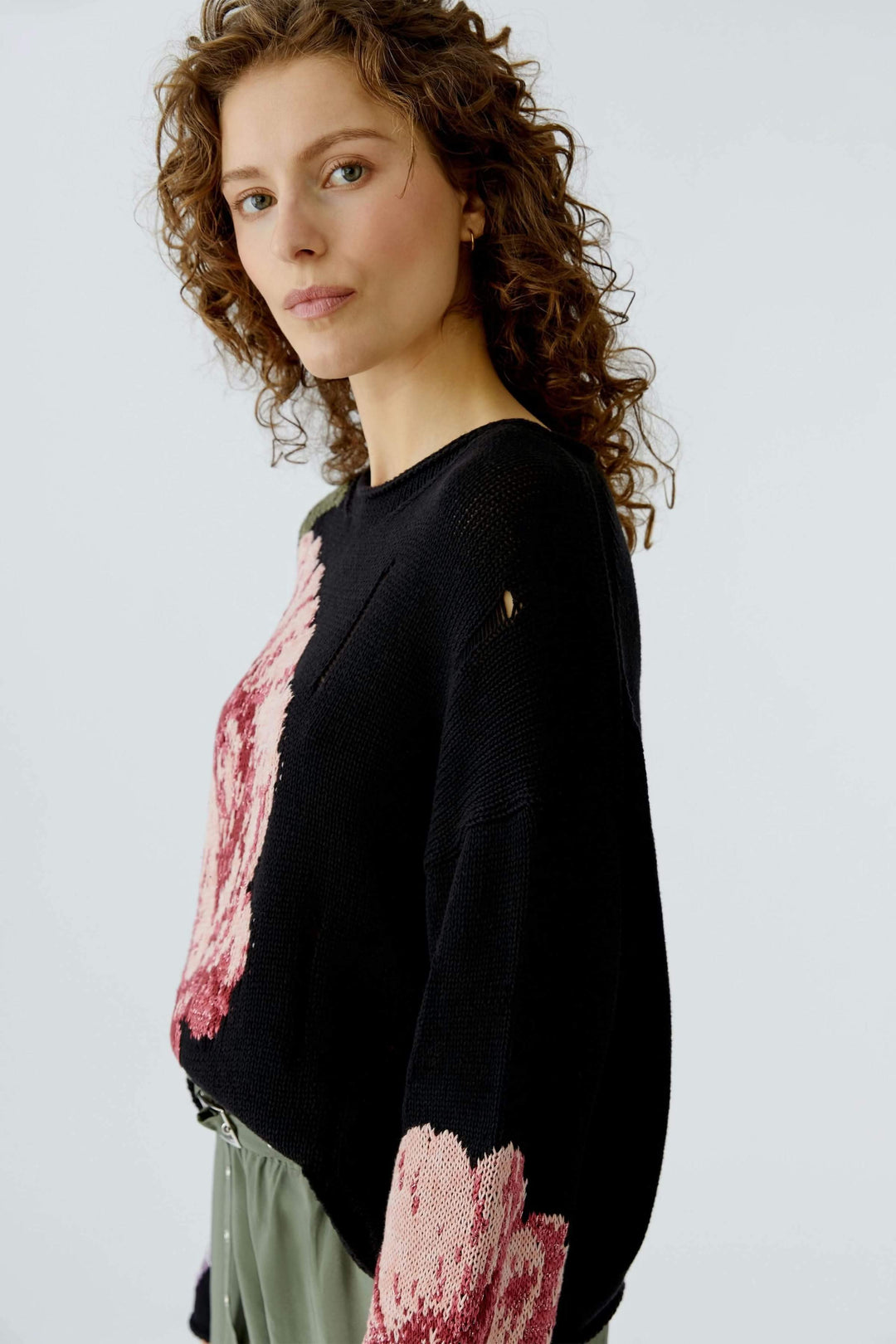 Femme portant un chandail imprimé floral noir avec motif artistique et détails ajourés, coupe décontractée et encolure arrondie.