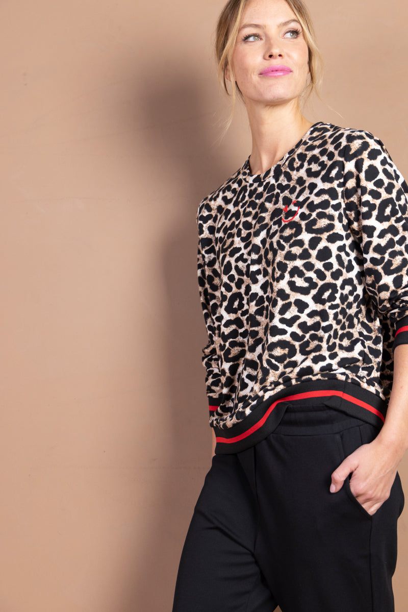 Femme portant un chandail imprimé léopard avec finitions sport chic, style polyvalent pour look moderne et affirmé.