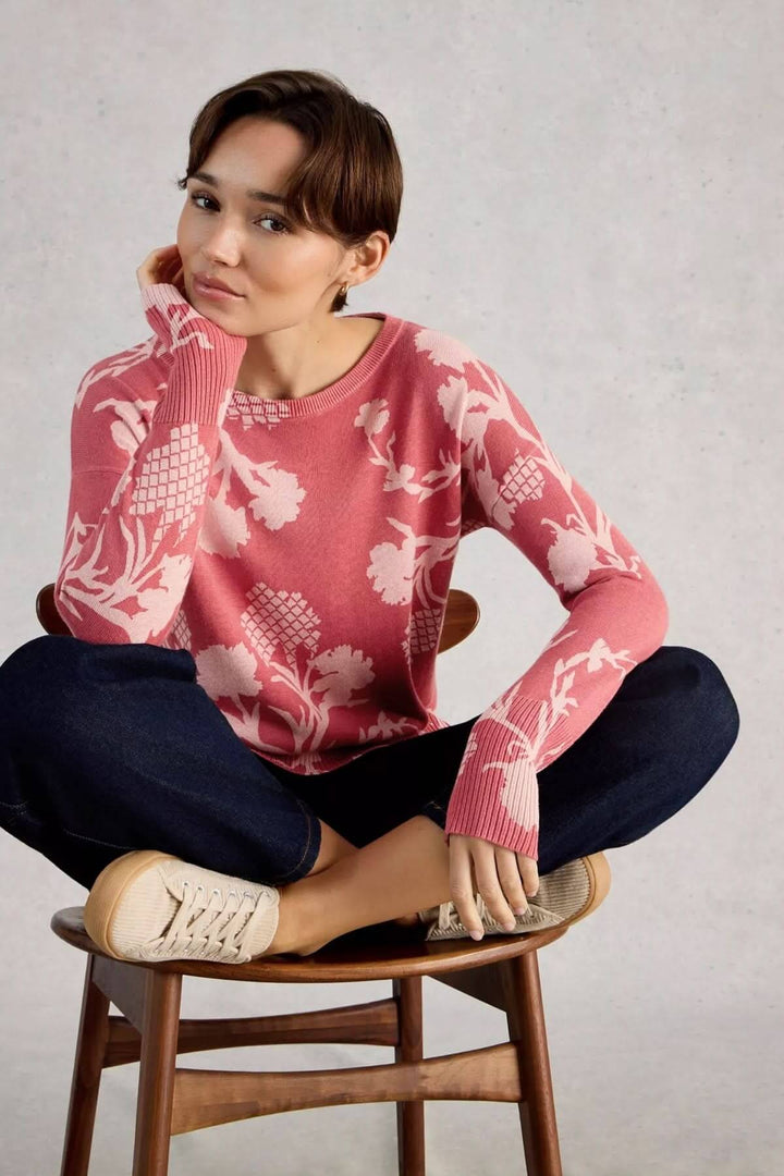 Femme portant un chandail imprimé à manches longues Olive, assise sur une chaise en bois, avec un motif floral, style décontracté.