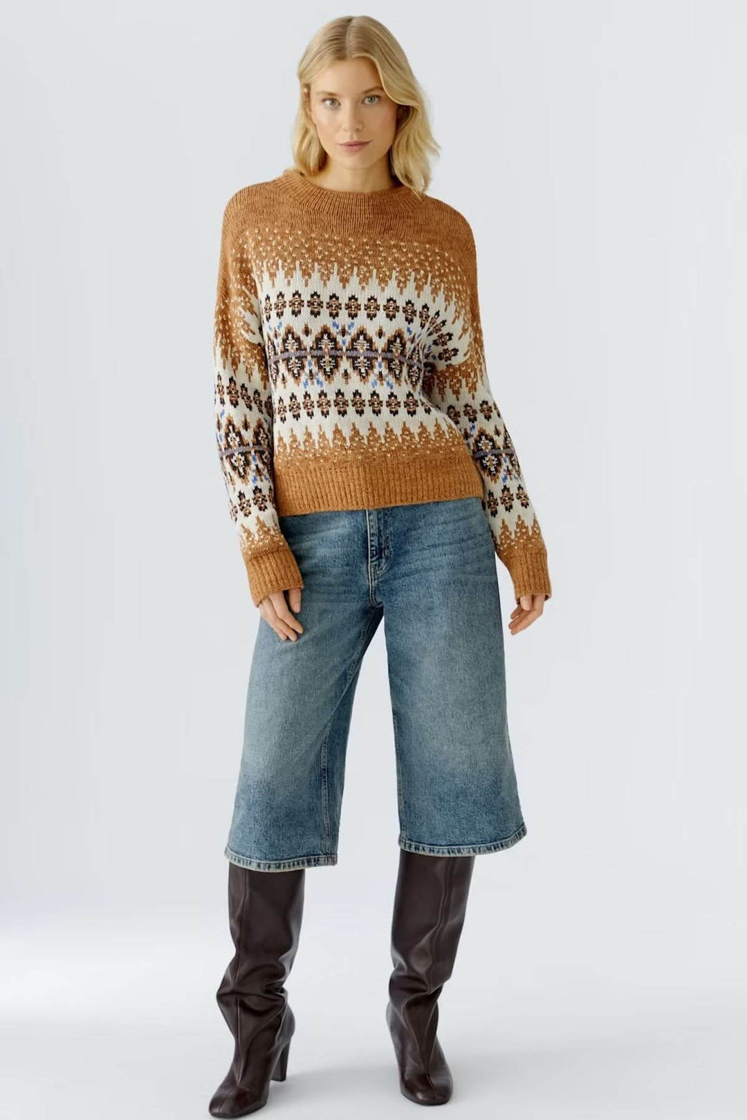 Femme portant un chandail jacquard à motif nordique avec un col montant, associé à un jean ample et des bottes hautes.