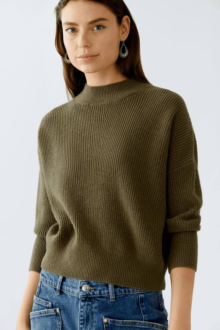 Femme portant un chandail maille fine à col montant avec finitions côtelées et coupe ample, allié à un jean pour un style chic.