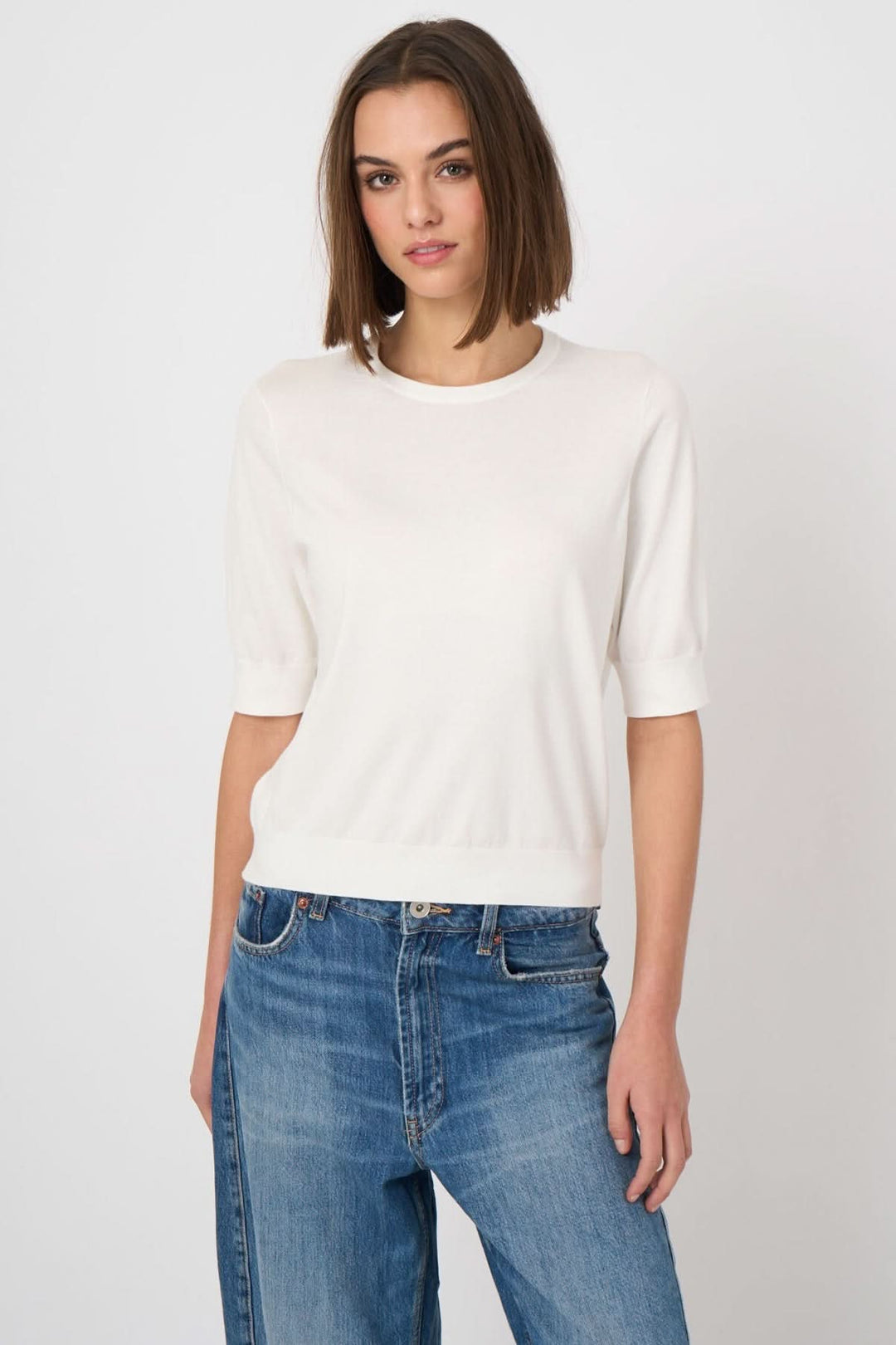 Femme portant un chandail à manches courtes blanc, coupe droite et encolure ronde, avec un jean bleu décontracté.