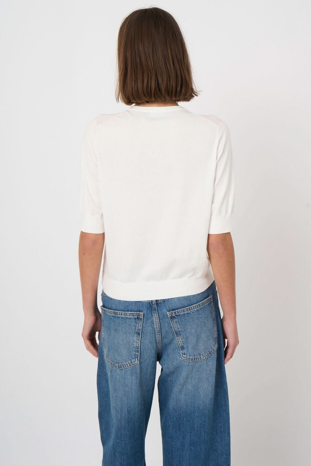 Dos d'une femme portant un chandail à manches courtes blanc élégant avec un jean décontracté.