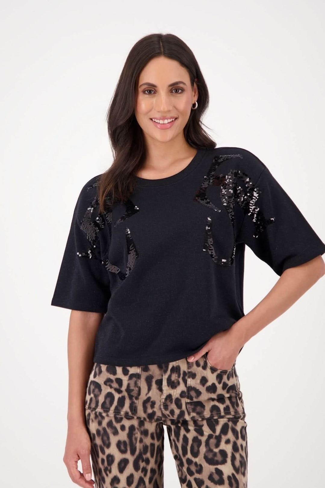Chandail noir à manches courtes avec appliqués de paillettes et motif abstrait, porté avec un pantalon léopard.