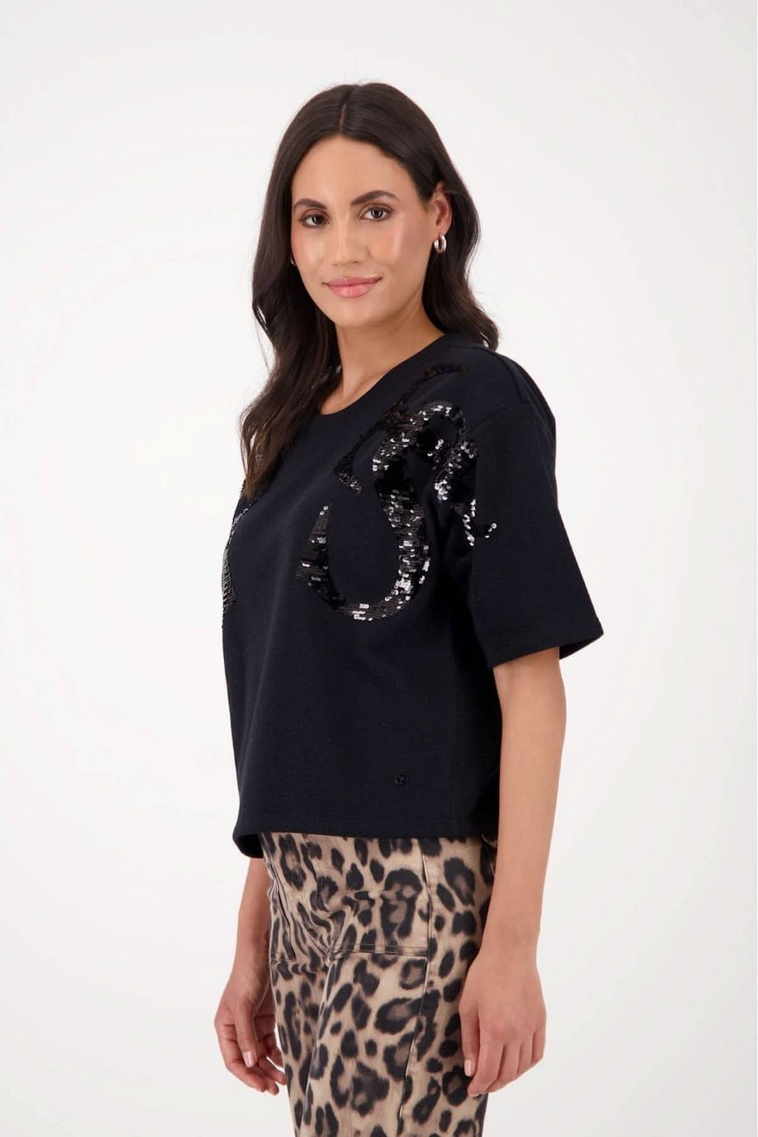 Chandail à manches courtes en maille noire avec motif abstrait en sequins, porté avec une jupe léopard.