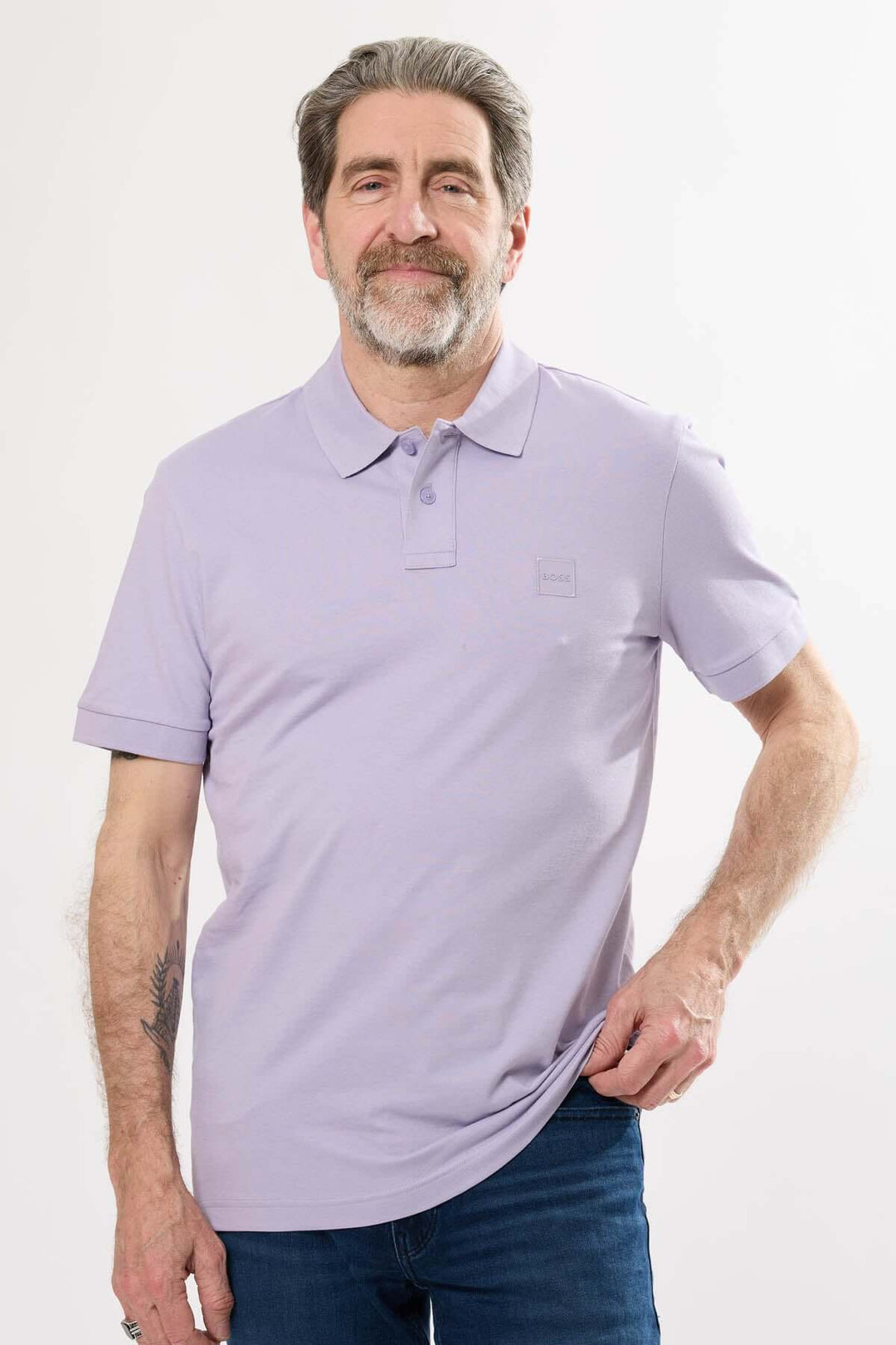 Homme souriant portant un polo lavande à logo discret BOSS, devant un fond blanc.