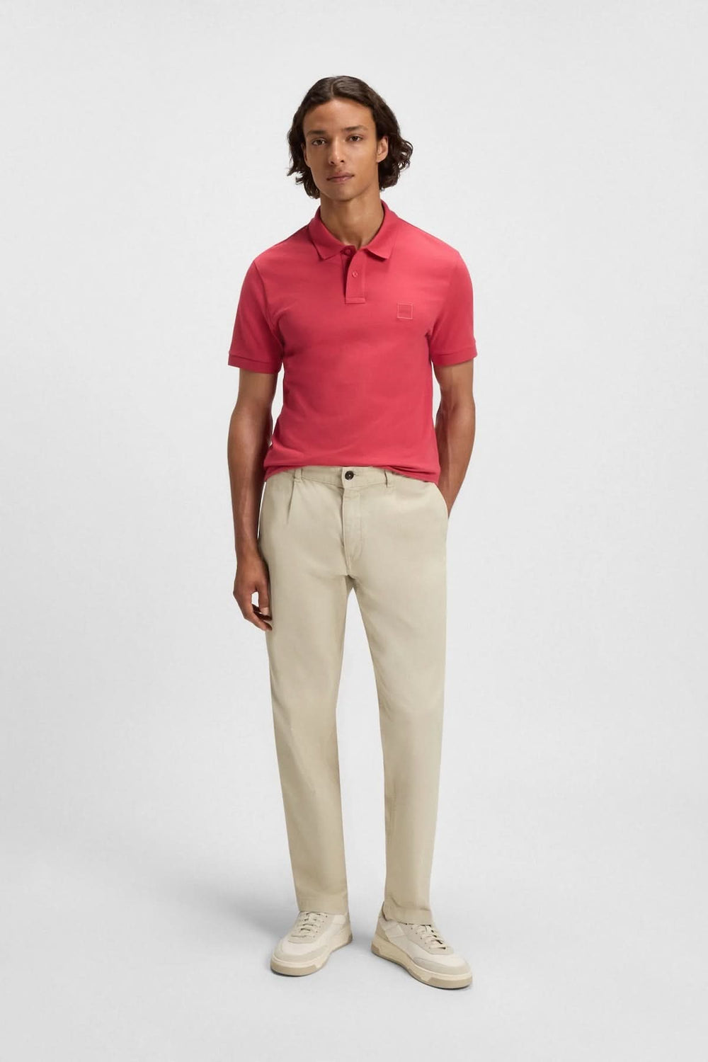 Homme portant un chandail polo rose à logo Boss avec pantalon clair et chaussures, affichant un style décontracté.