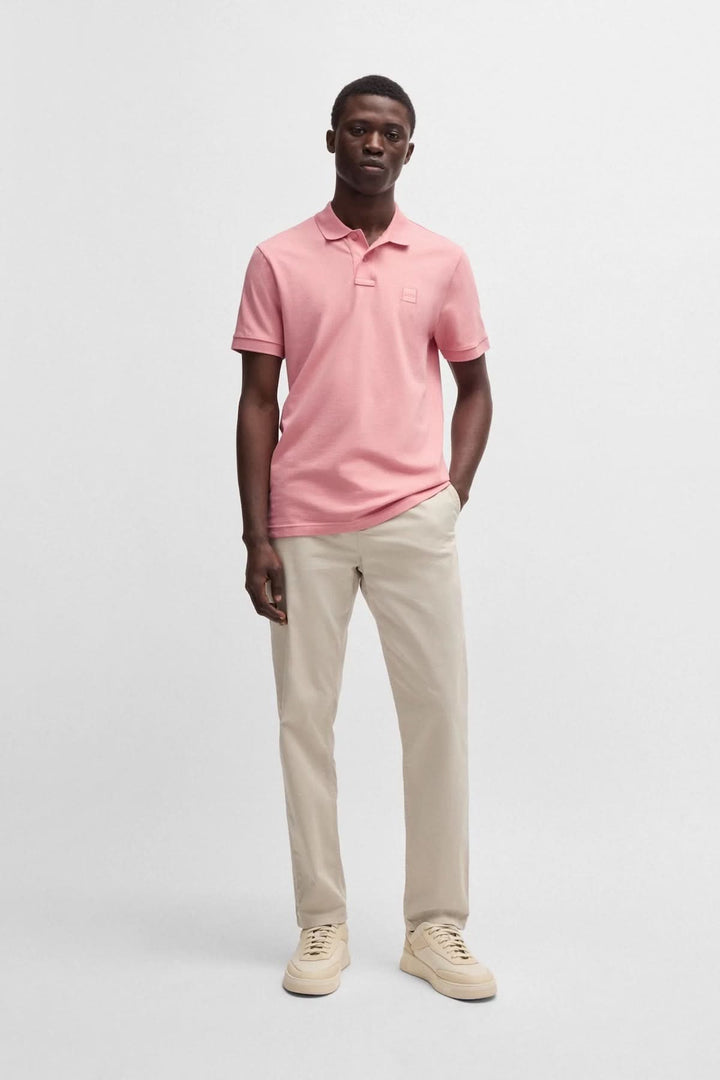 Homme portant un polo rose BOSS avec un logo discret, associé à un pantalon beige et des chaussures claires.
