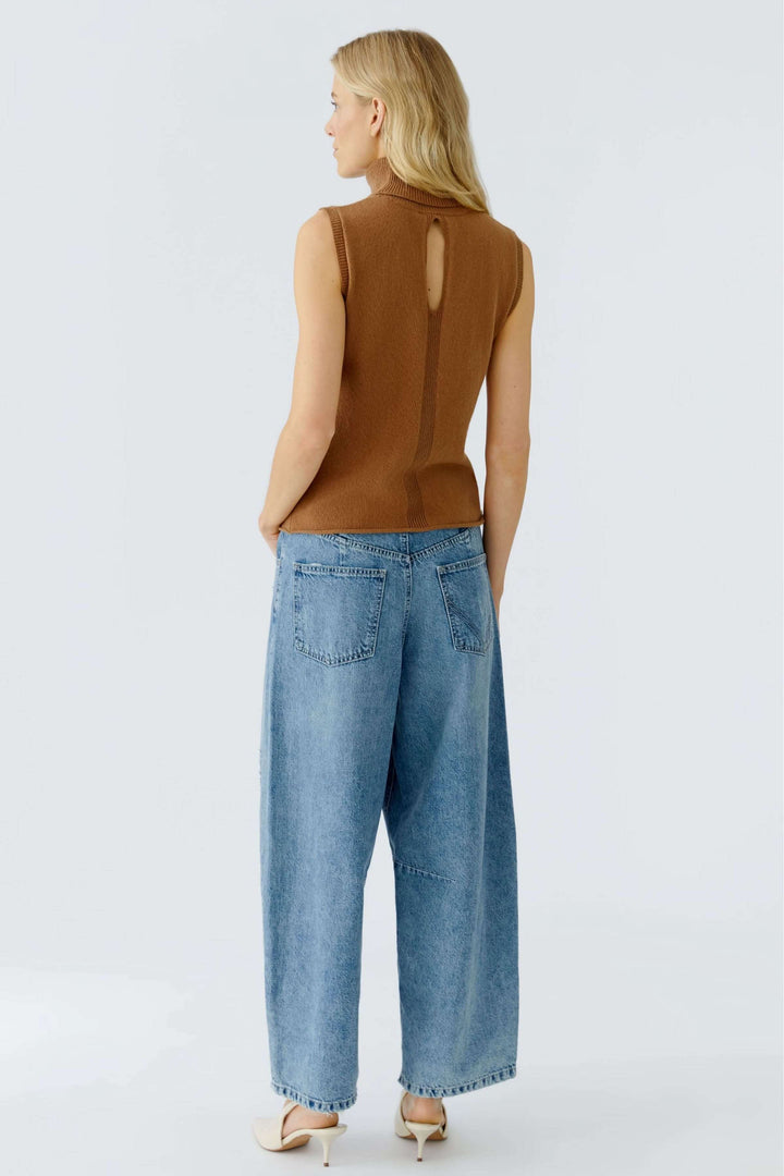 Chandail sans manches à col roulé, dos ajouré, porté avec un jean large pour un look minimaliste et moderne.
