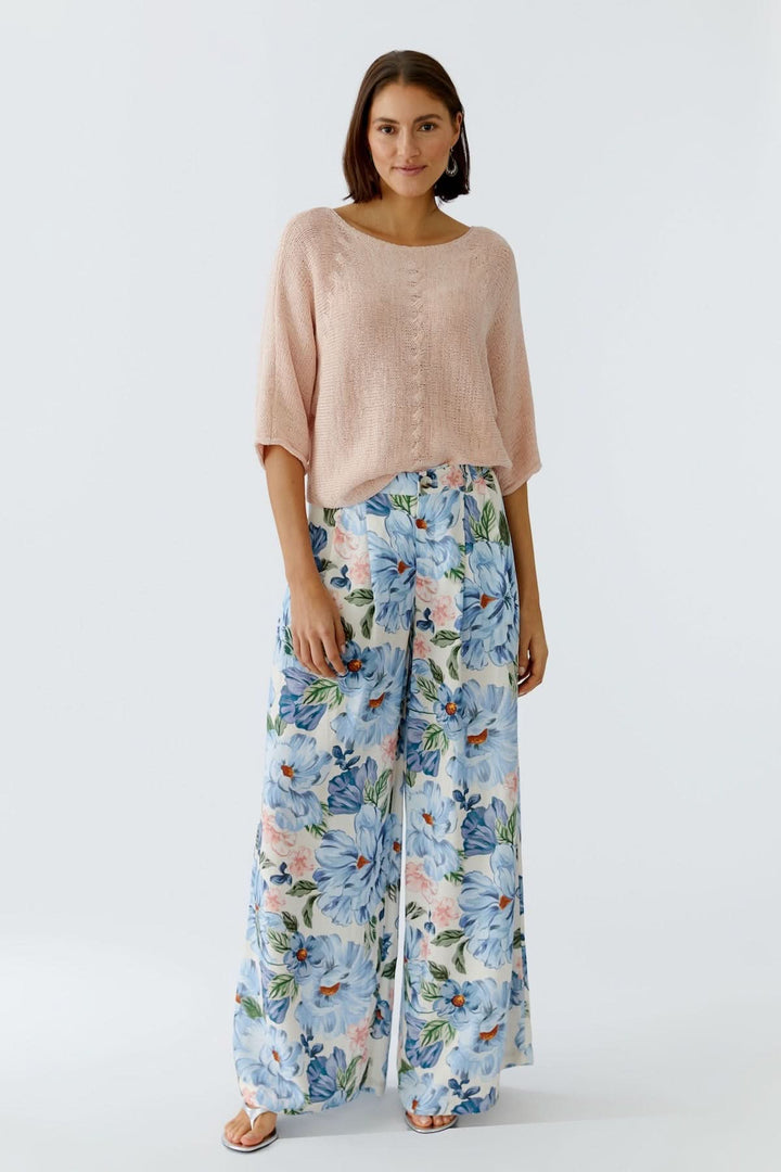 Femme portant un chandail tricot léger et pantalon à motifs floraux, offrant une silhouette décontractée et moderne.