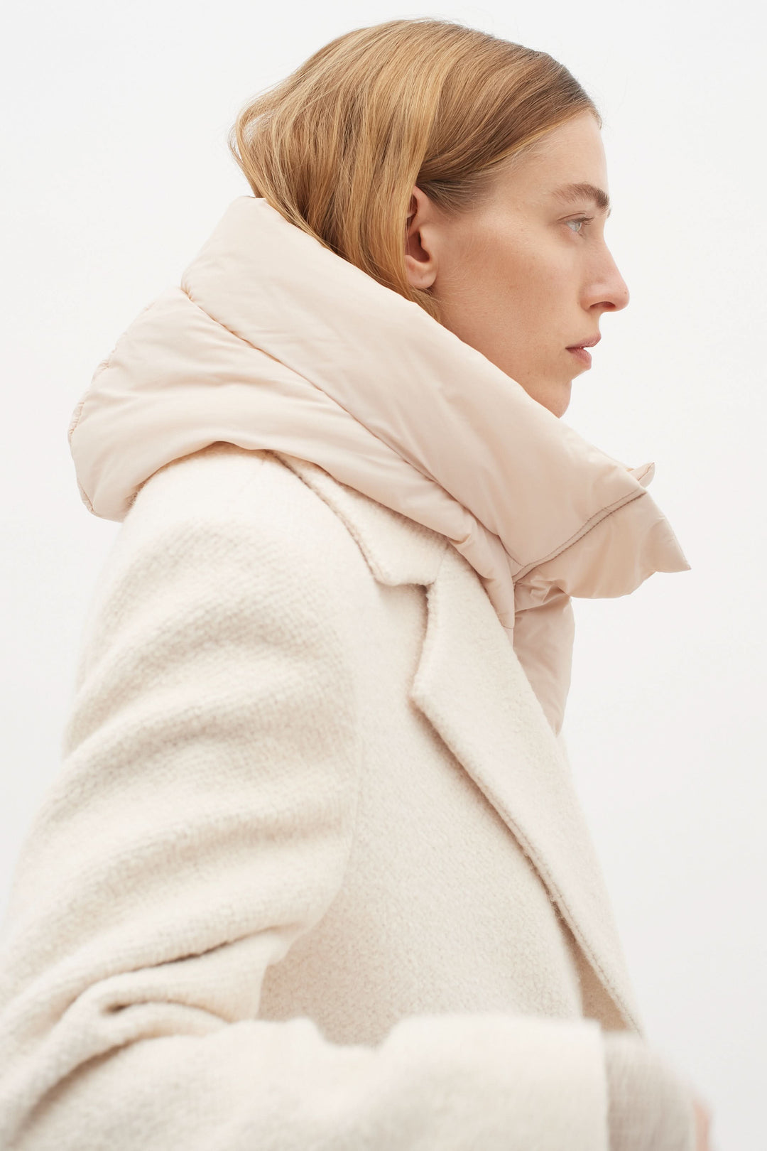 Femme avec une capuche matelassée rose portée sur un manteau blanc, idéale pour les temps froids.