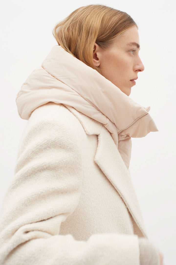 Femme avec une capuche matelassée rose portée sur un manteau blanc, idéale pour les temps froids.