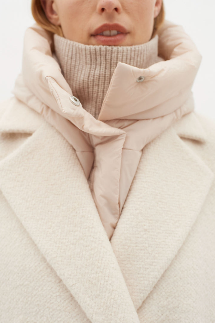 Modèle portant une capuche matelassée élégante sur un manteau beige, parfaite pour l'hiver.