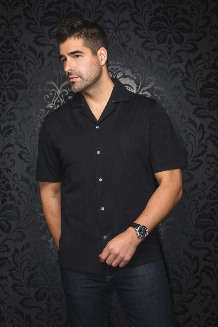 Homme portant une chemise à manches courtes noire, style cubain, devant un fond texturé noir.
