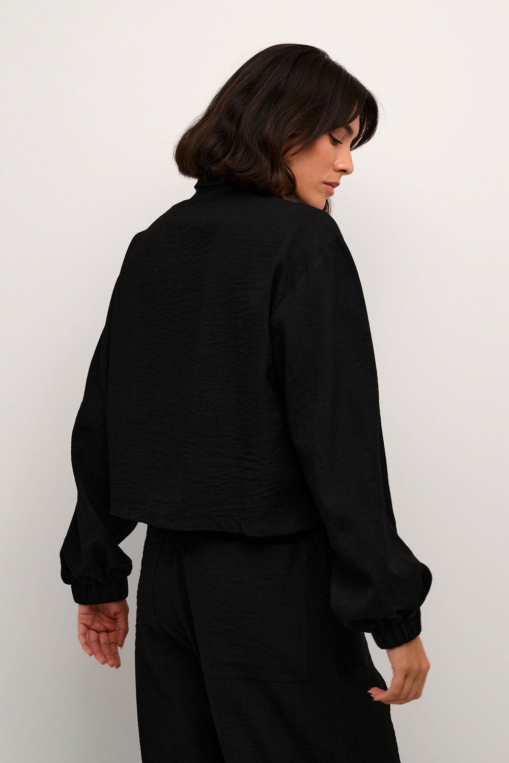 Femme portant une chemise noire à manches bouffantes, vue de dos, style décontracté.