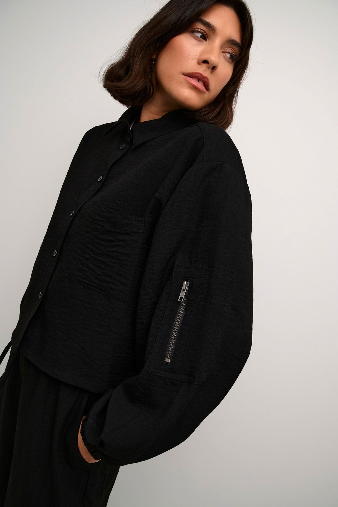 Chemise Elenor noire à manches longues avec boutonnière et fermeture éclair sur la manche pour un look élégant.