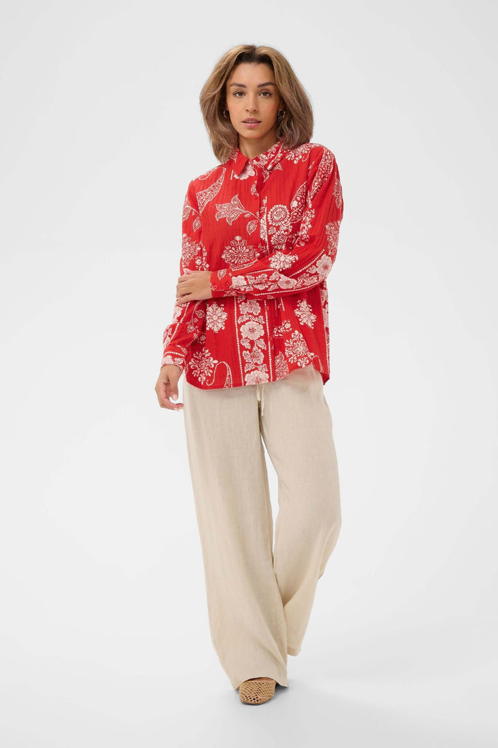 Femme portant une Chemise Gianna imprimée à manches longues rouges avec motifs, et pantalon beige fluide.