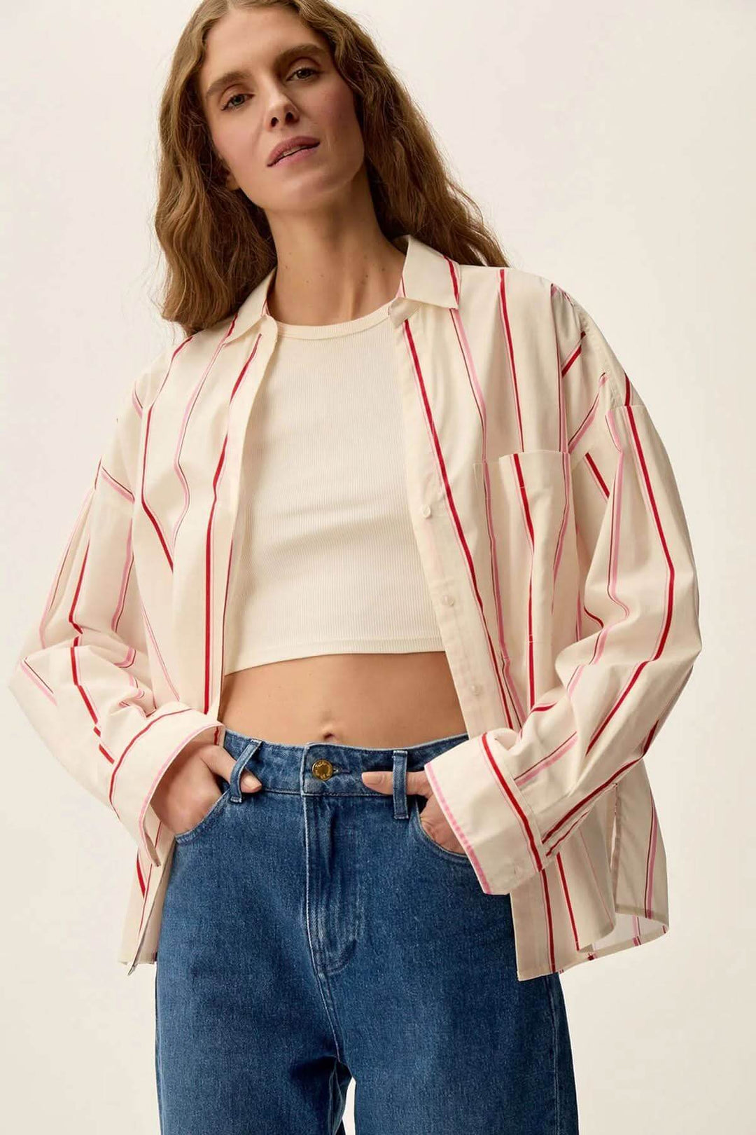Femme portant une chemise blanche à rayures rouges, parfaite pour un look décontracté avec un jean.