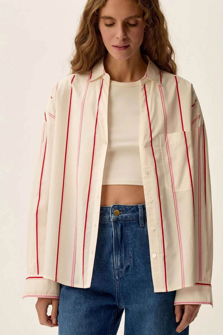Chemise blanche à rayures rouges, manches longues, col V, portée avec un jean, style élégant et décontracté.