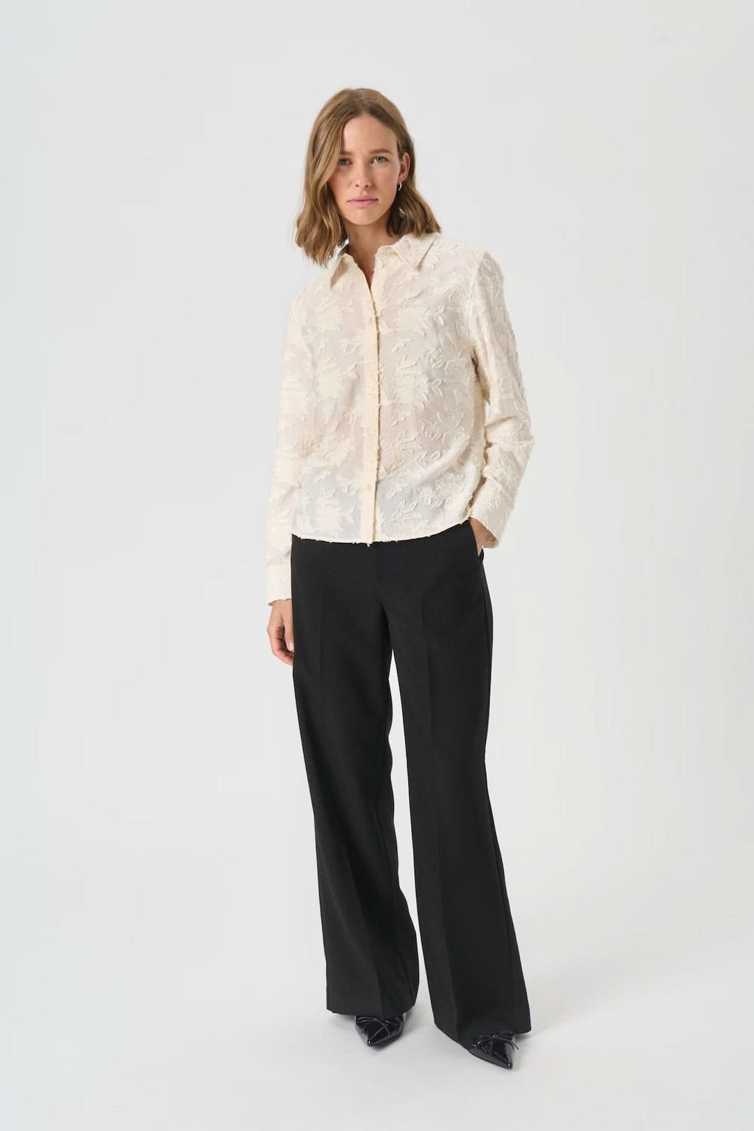 Femme portant la chemise Vilya à relief floral ton sur ton, semi-transparente avec manches longues, élégance et confort en viscose.