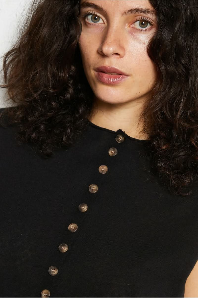 Femme portant un haut noir avec boutons, regard direct.