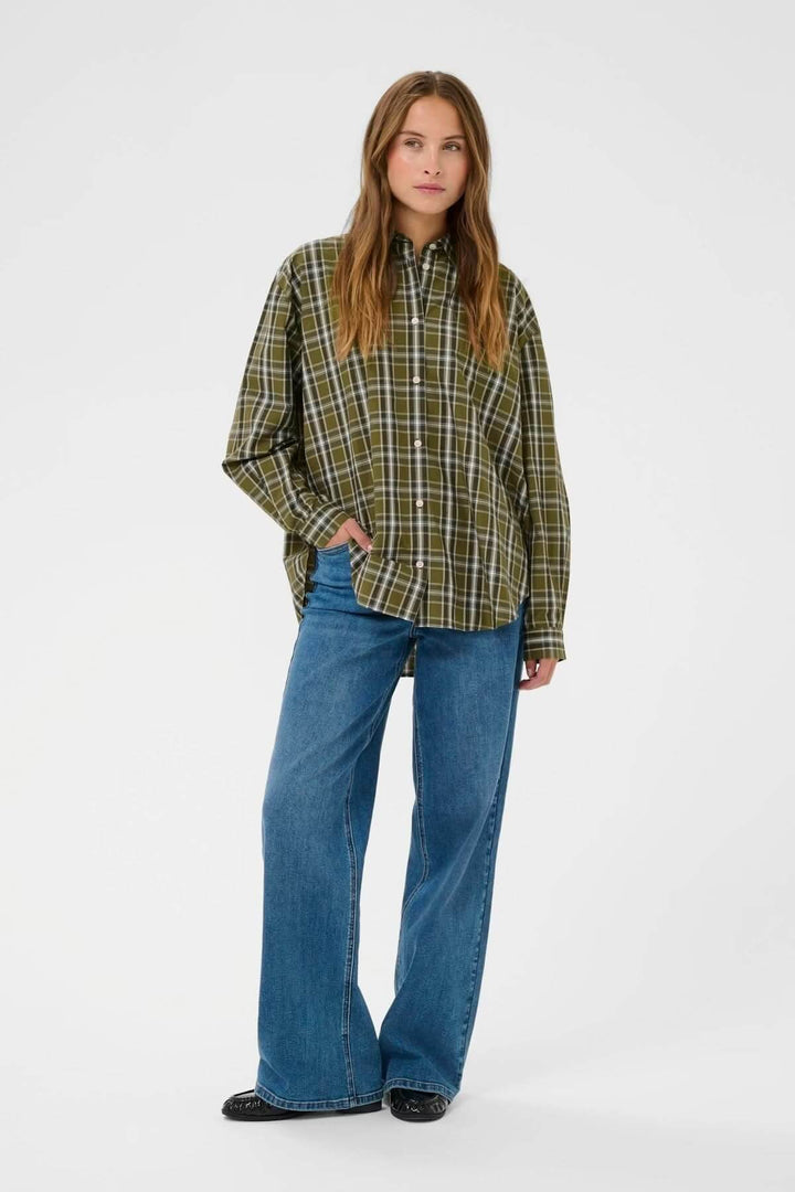 Femme portant une chemise à carreaux verte, coupe décontractée, avec un jeans évasé bleu pour un look casual chic.