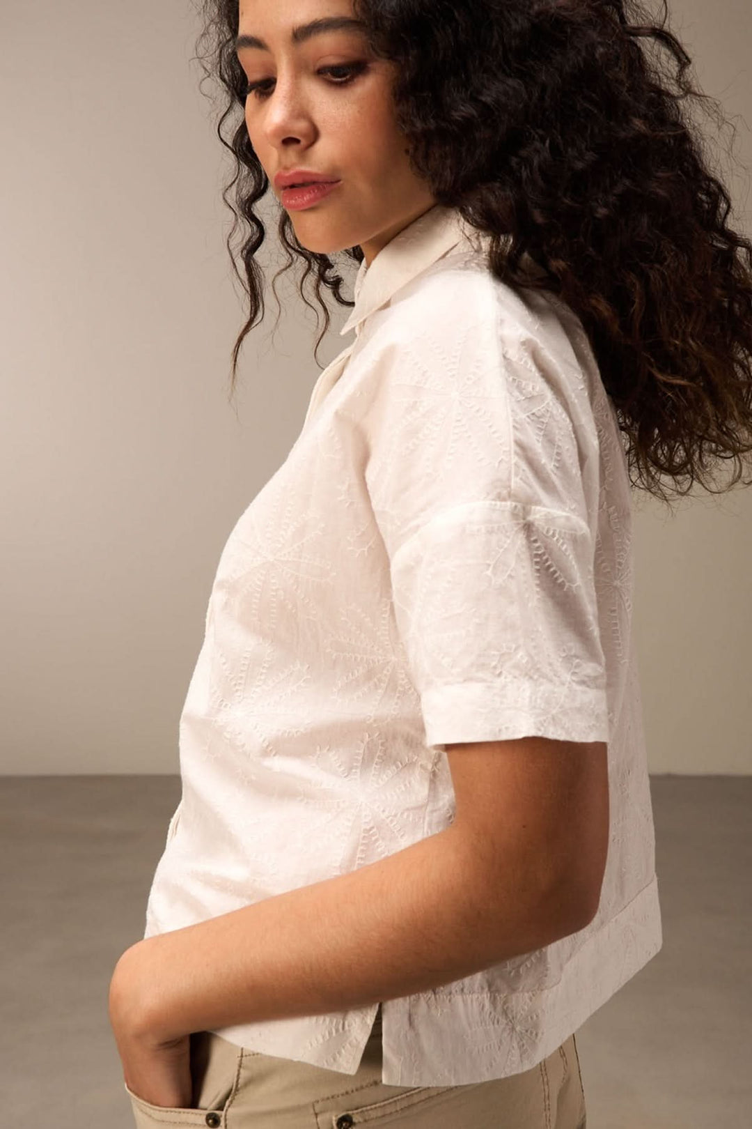 Chemise courte à manches courtes avec broderie florale sur fond blanc, portée de côté par une femme.