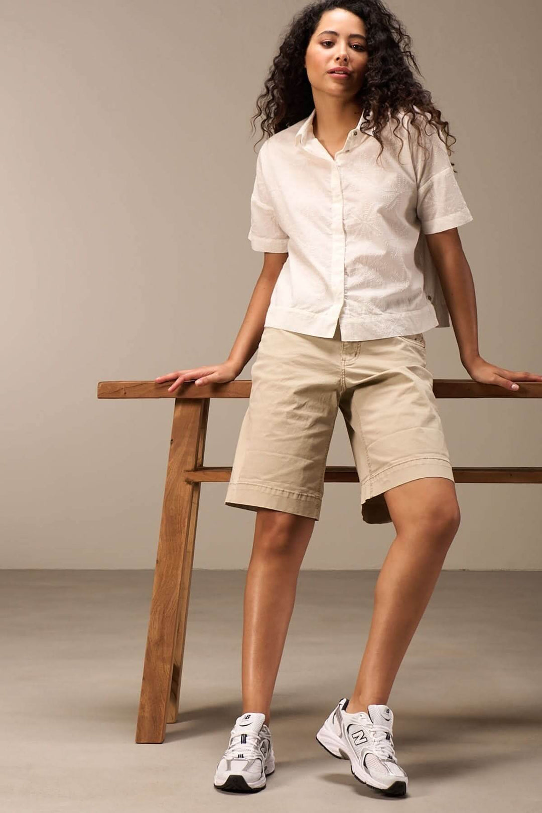 Femme portant une chemise courte à manches courtes et un short beige, posant avec des sneakers blanches.