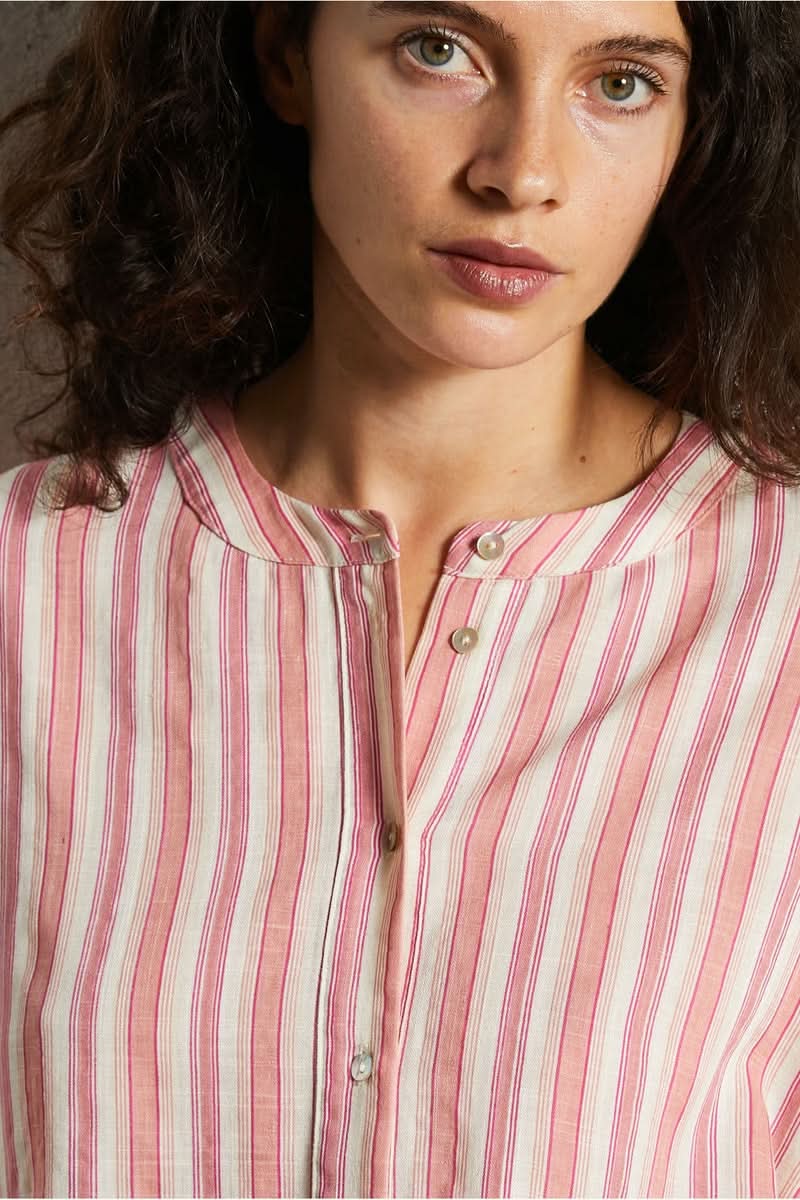 Femme portant une chemise design épuré avec rayures roses et blanches, style moderne et intemporel, coupe droite et fermeture boutonnée.