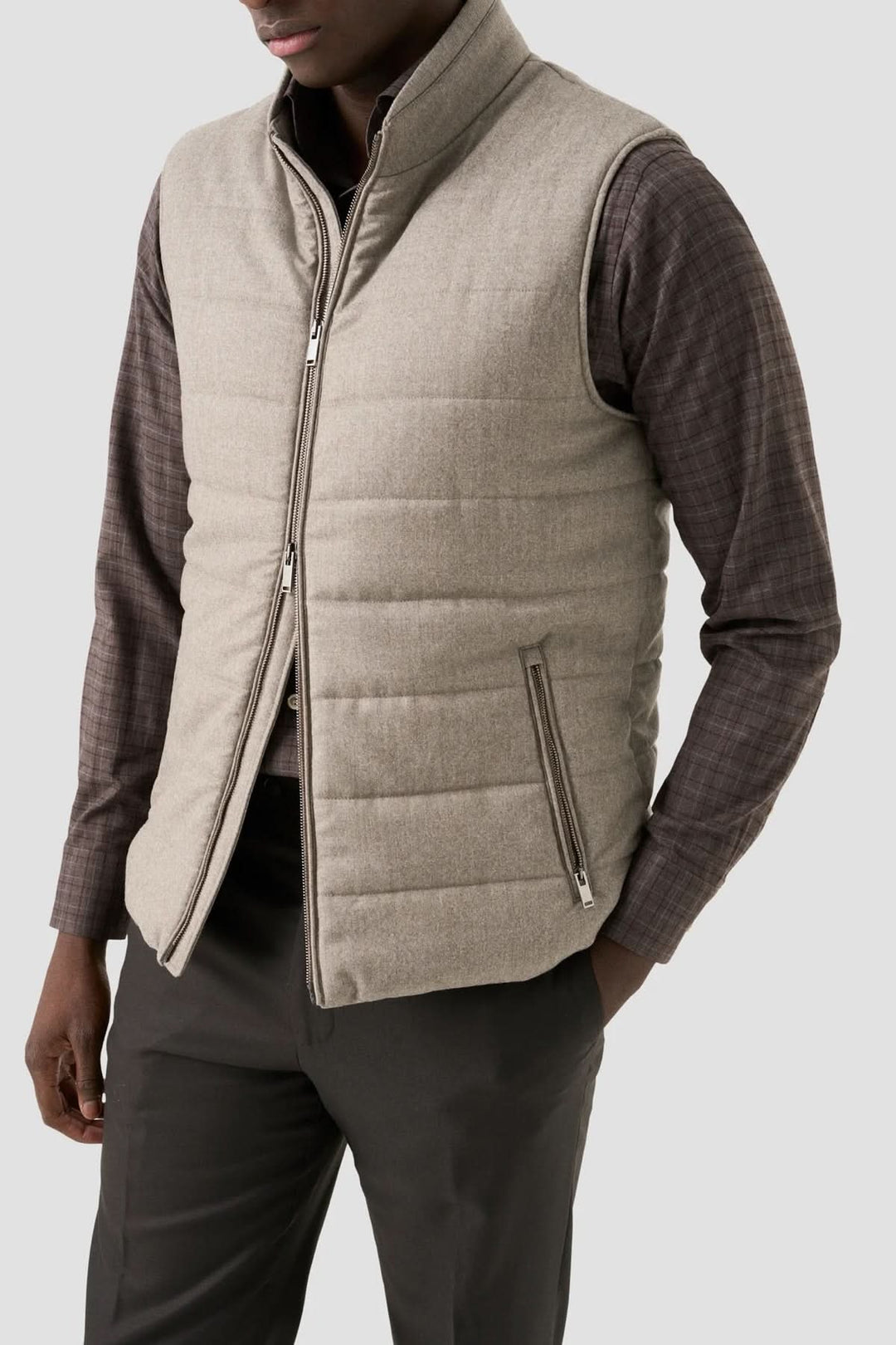 Gilet matelassé beige porté avec chemise à carreaux et pantalon noir, pour un look moderne et élégant.