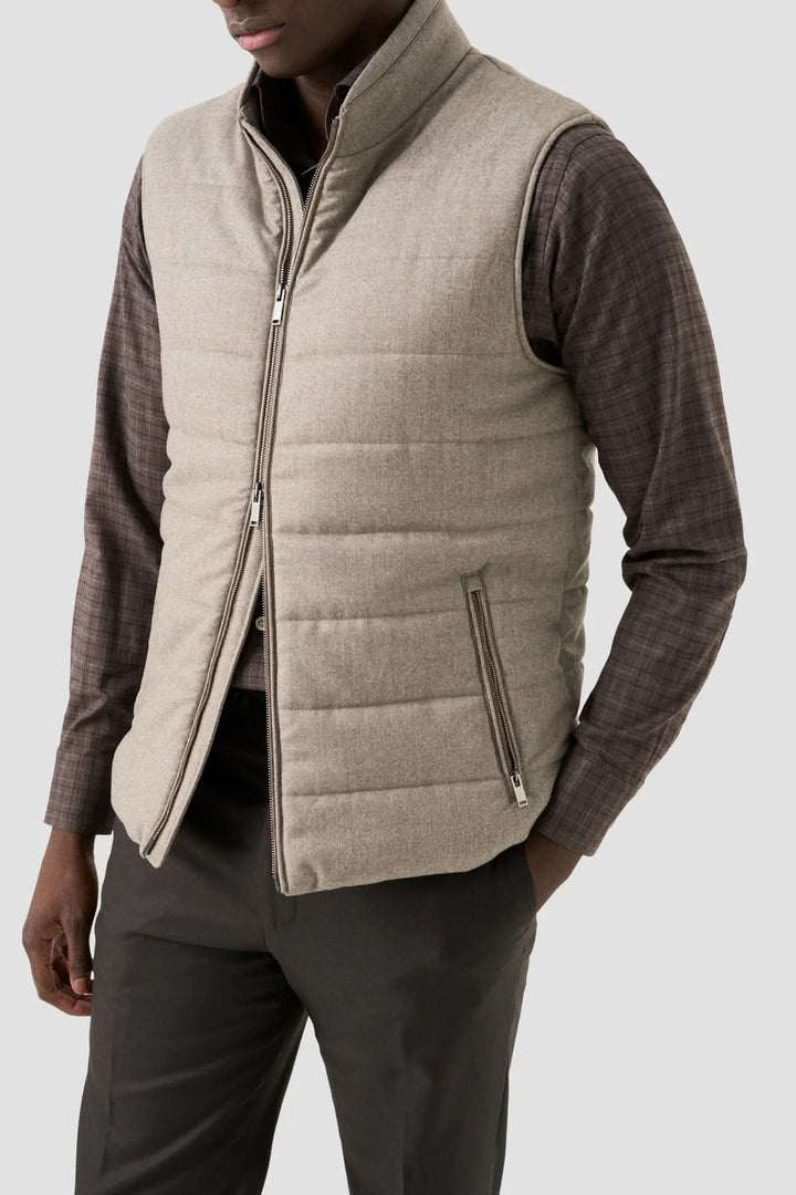 Gilet matelassé beige porté avec chemise à carreaux et pantalon noir, pour un look moderne et élégant.