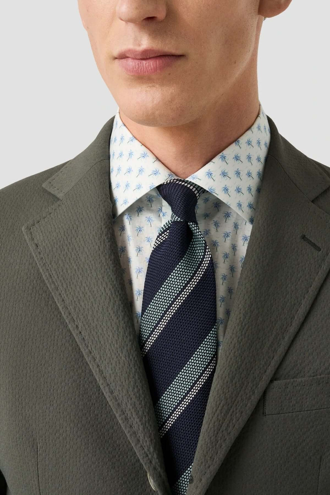 Homme portant une chemise en sergé à motif palmier et une cravate à rayures, sous un blazer élégant.