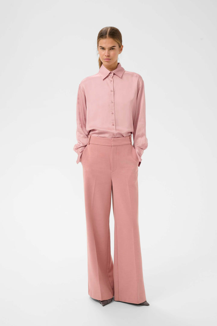 Modèle portant la Chemise fluide Pauline rose avec un pantalon assorti, élégant et moderne, intérieur studio.