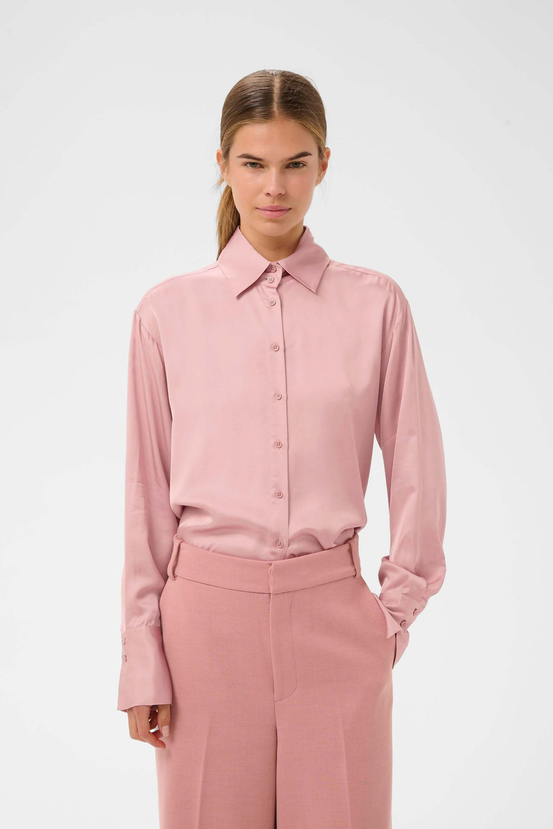 Femme portant la Chemise fluide Pauline rose, coupe droite et fluide avec col classique, idéale pour un style élégant et polyvalent.