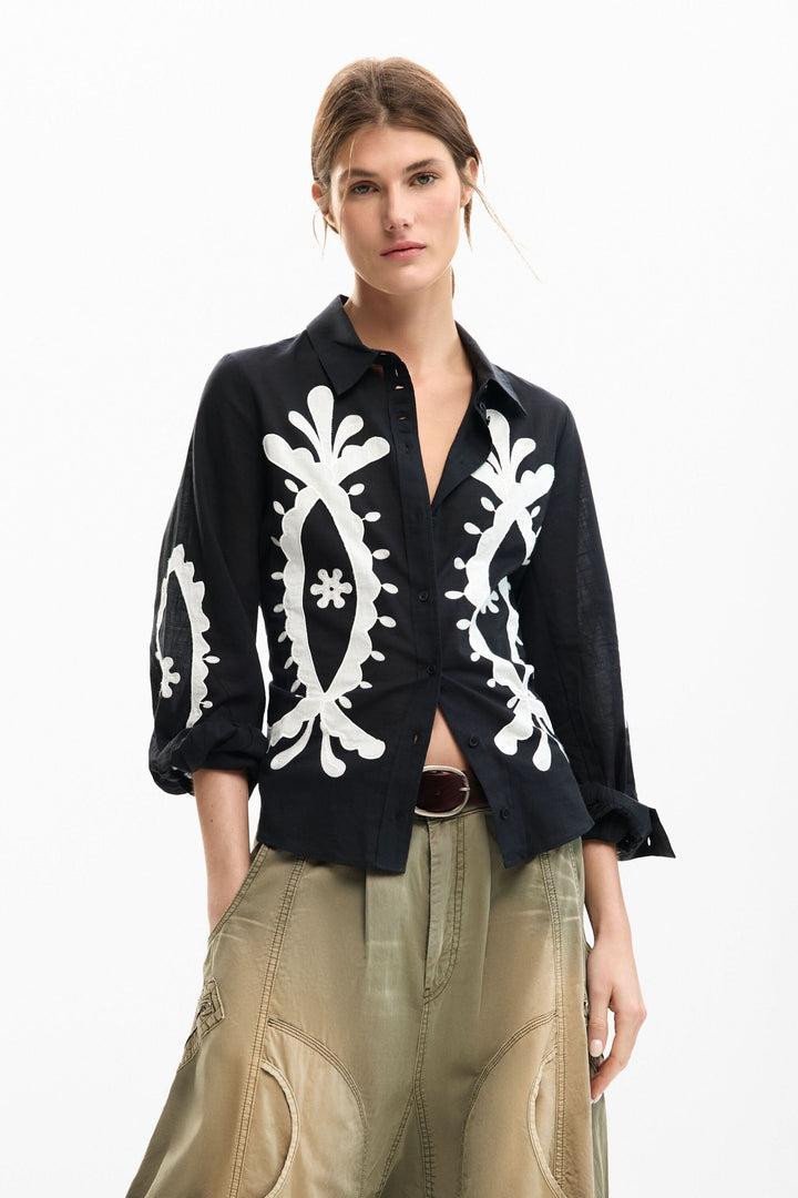 Chemise fluide à broderies contrastées sur mannequin portant un pantalon kaki, style élégant et décontracté.