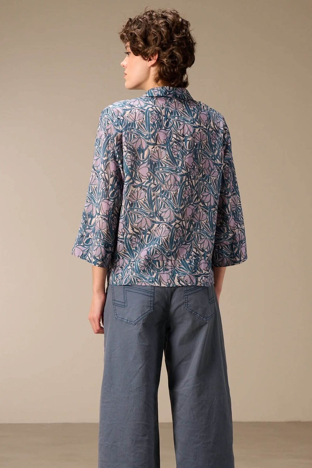 Modèle portant une chemise fluide à manches trois-quarts avec imprimé, vue de dos, montré avec un pantalon large bleu.
