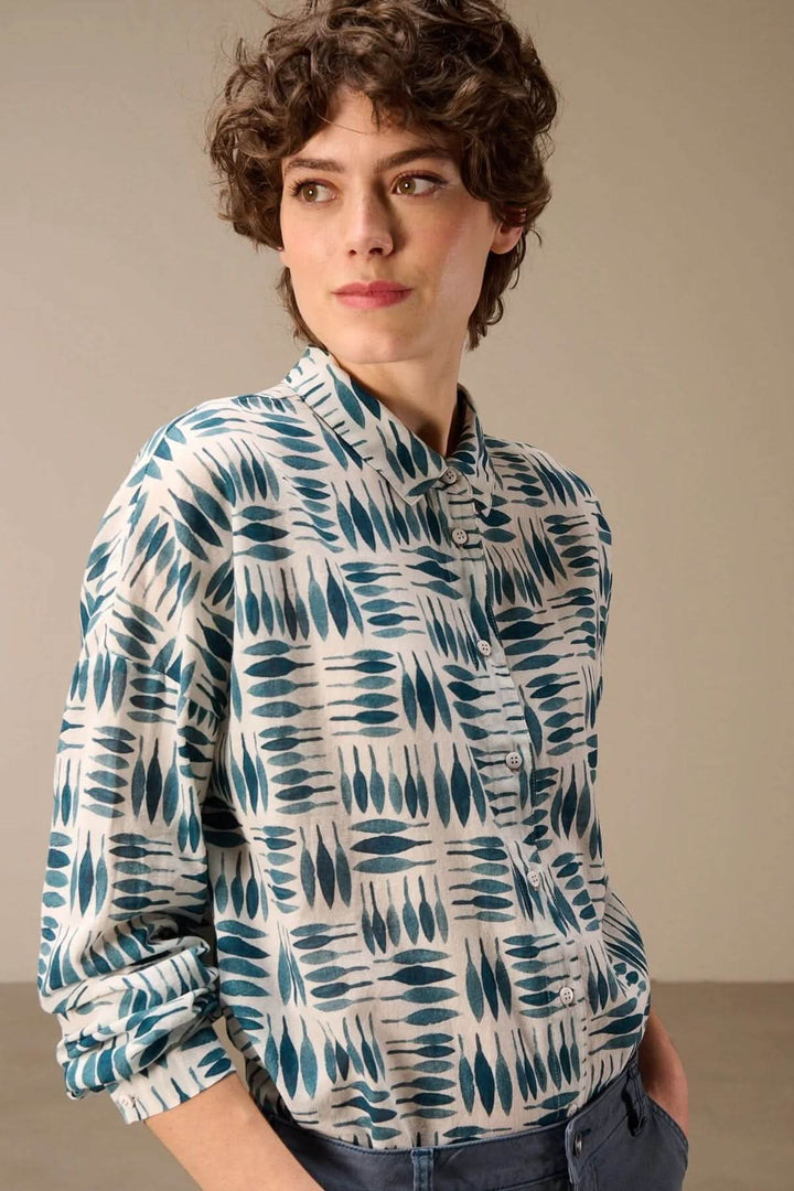 Femme portant une chemise imprimée à manches longues avec un imprimé graphique bleu et blanc, style moderne et confortable.