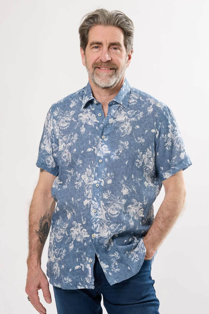 Homme souriant portant une chemise à manches courtes à motif floral sur fond chambray, idéal pour l'été.