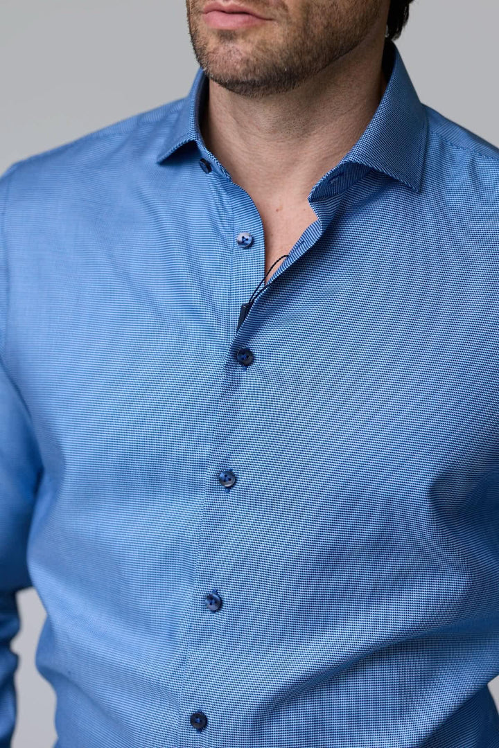 Homme portant une chemise à micro-motif texturé bleu, manches longues, col classique, coupe ajustée.