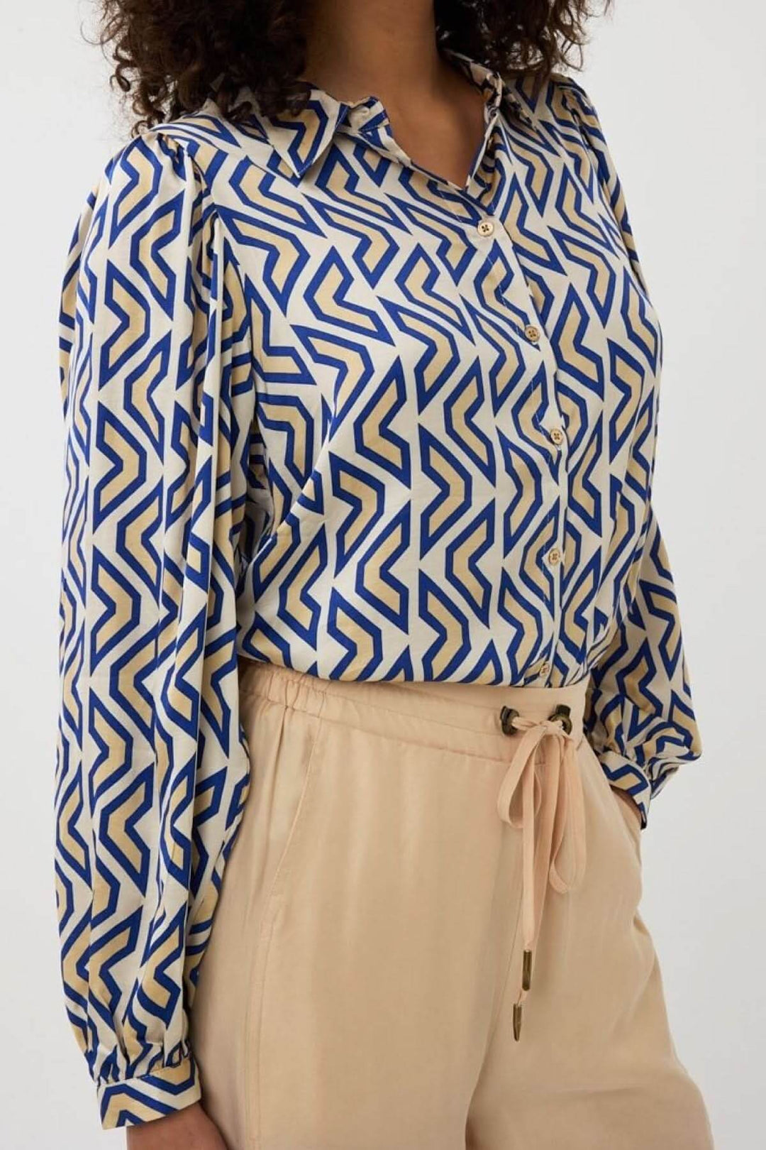 Chemise à motif géométrique bleue et beige avec col classique et manches longues, portée avec un pantalon.
